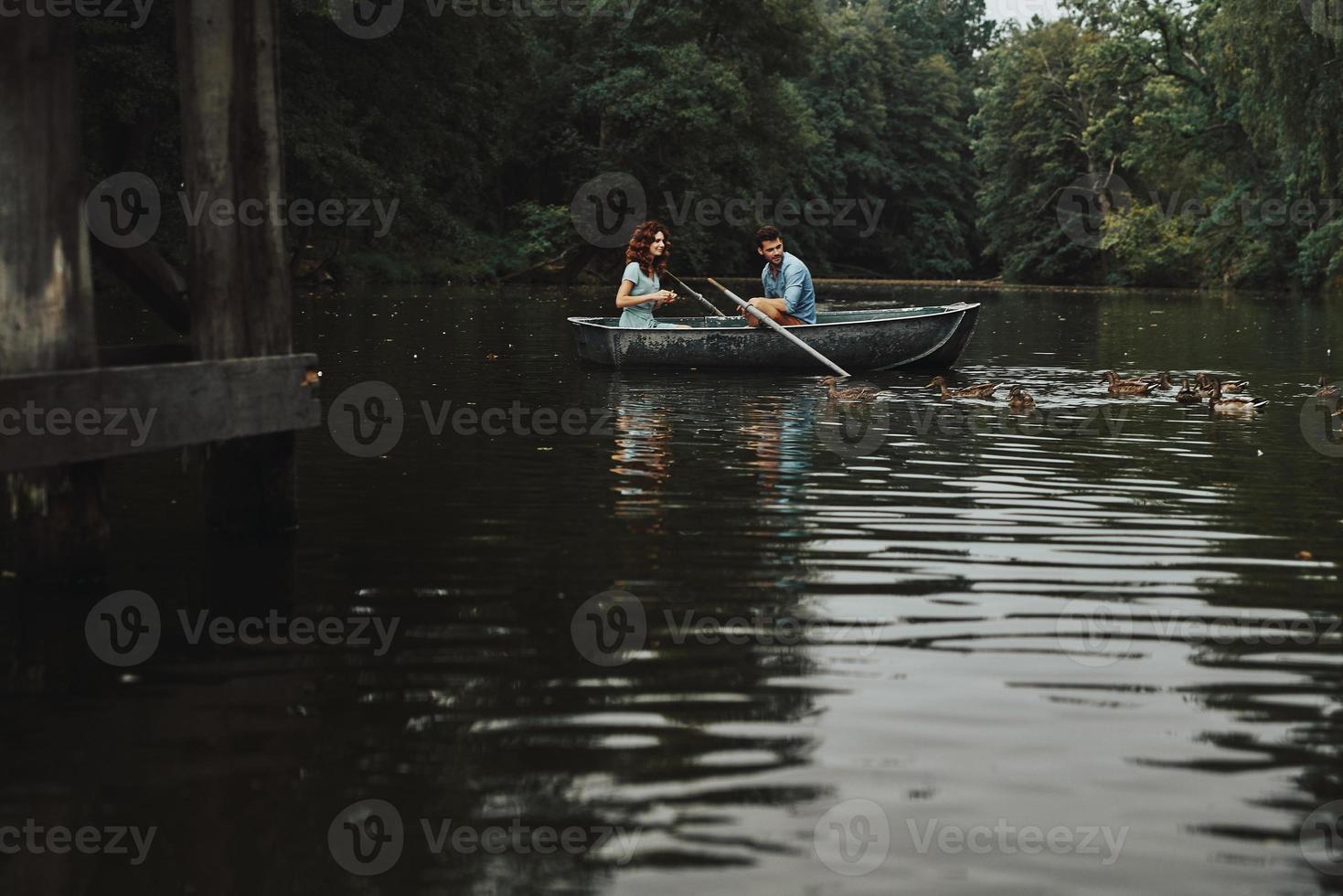 amor verdadero. hermosa pareja joven sonriendo y alimentando patos mientras disfruta de una cita romántica en el lago foto