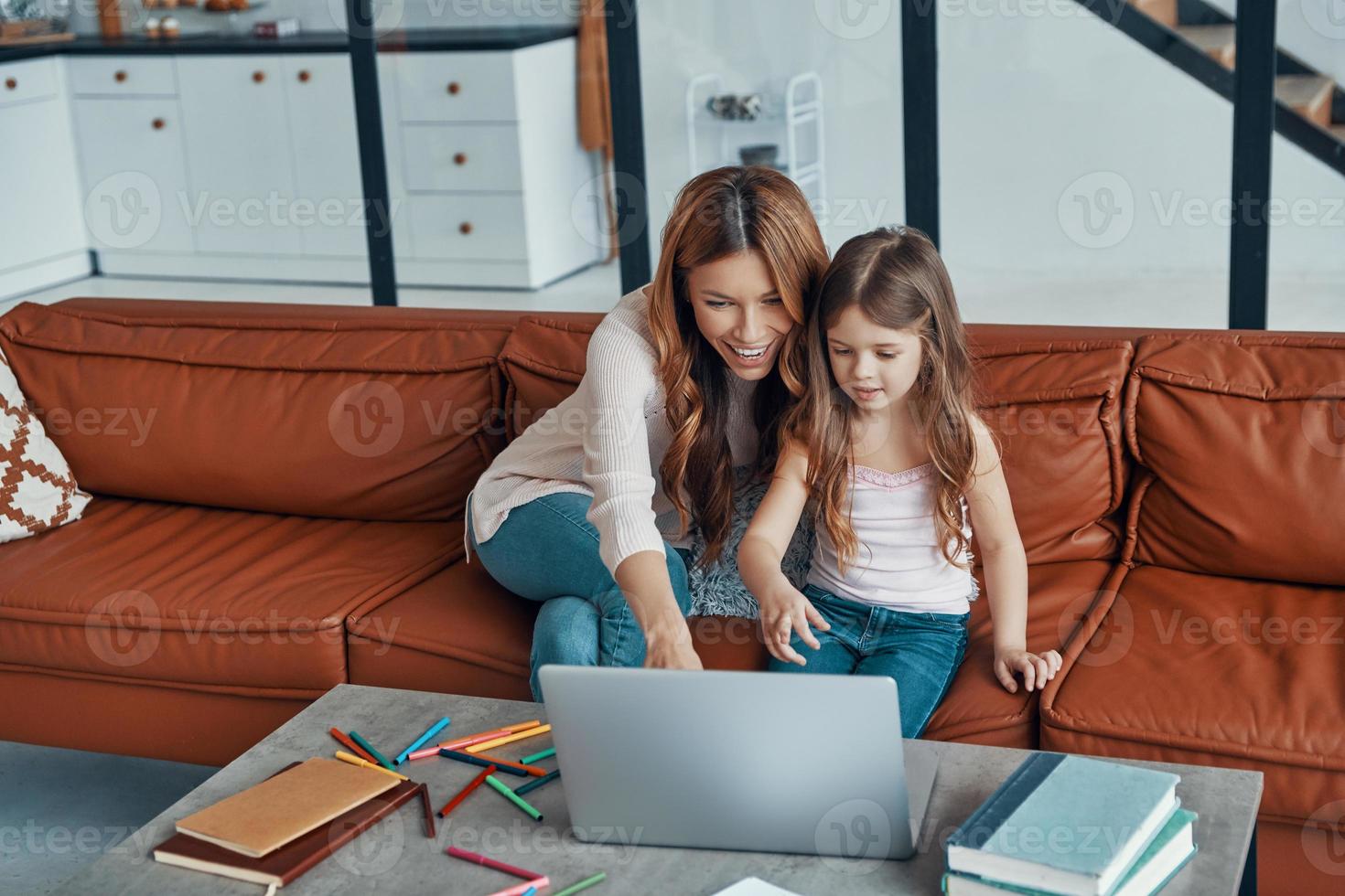 Young beautiful mother and her little daughter bonding together and smiling while using laptop at home photo