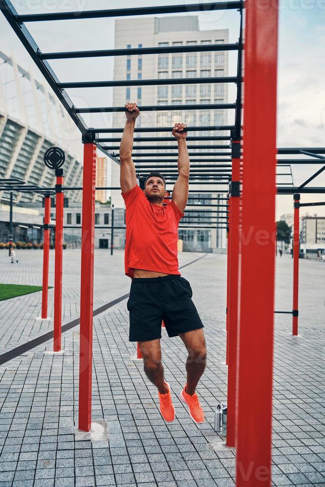 toda la longitud de un joven apuesto con ropa deportiva haciendo ejercicios mientras hace ejercicio al aire libre en la calle de la ciudad foto