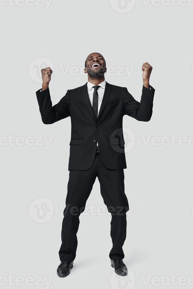 Full length of happy young African man in formalwear cheering while standing against grey background photo