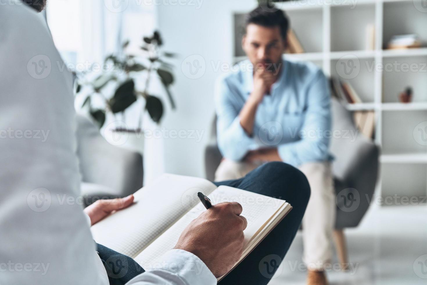 Making profile. Young frustrated man solving his mental problems while having therapy session with psychologist photo