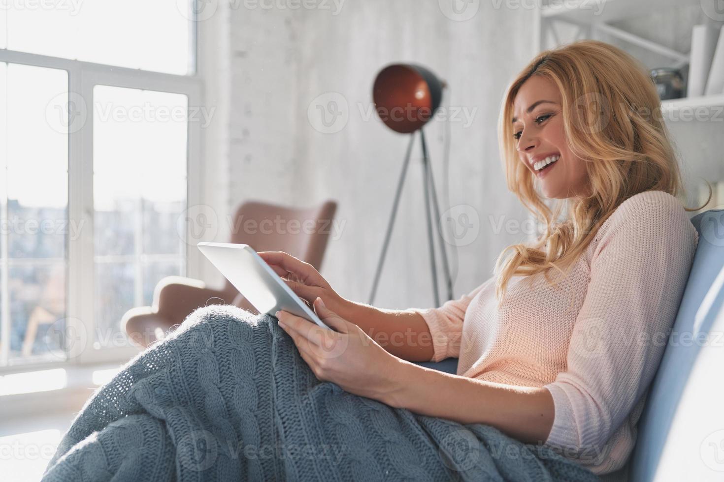 examinando su nueva tableta. mujer joven atractiva que usa una tableta digital y sonríe mientras se sienta en el sofá en casa foto