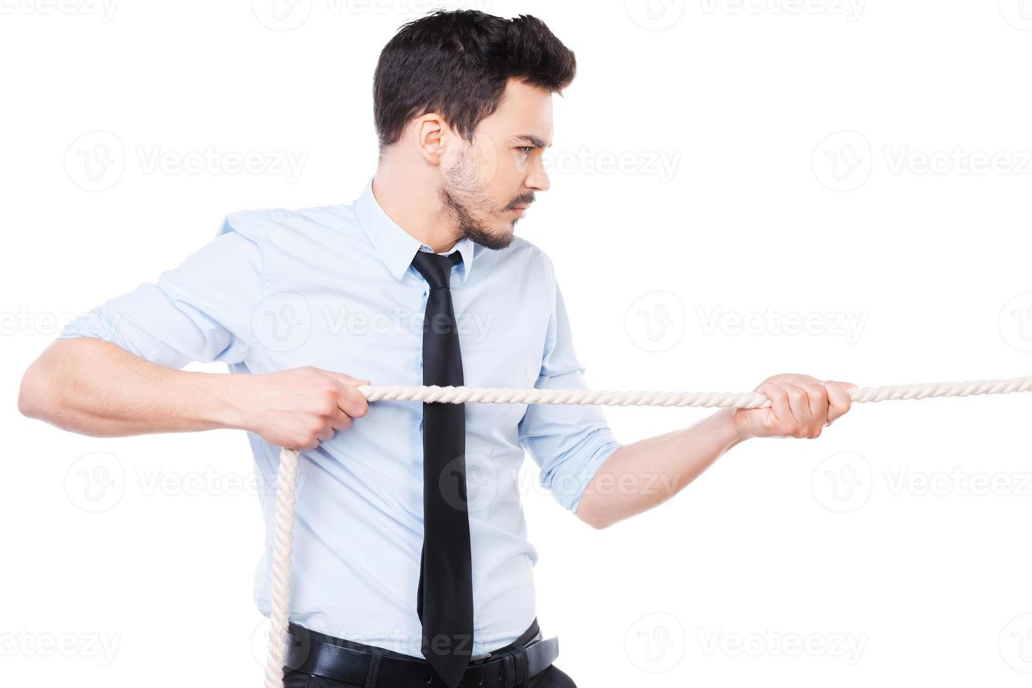 líder empresarial fuerte y confiado. vista lateral de un joven confiado con camisa y corbata tirando de una cuerda mientras se enfrenta a fondo blanco foto