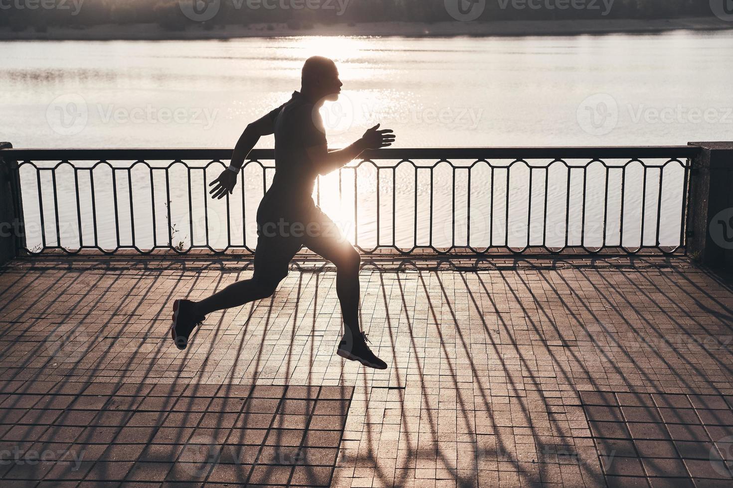 Training to become the best. Full length of young African man in sports clothing jogging while exercising outdoors photo