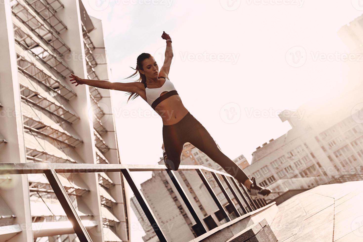 Everything is possible. Full length of modern young woman in sports clothing jumping while exercising outdoors photo