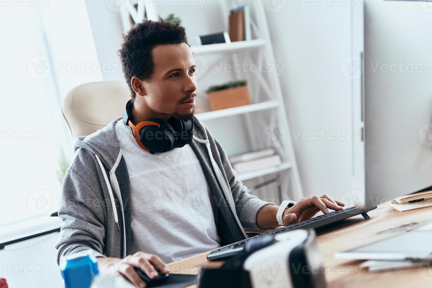 Computer hacker. Concentrated young man in casual clothing using computer while spending time at home photo