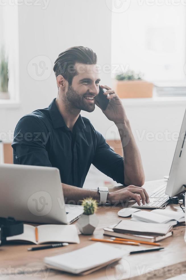 Pleasant talk. Handsome young man talking on the mobile phone while sitting at his working place in creative office photo