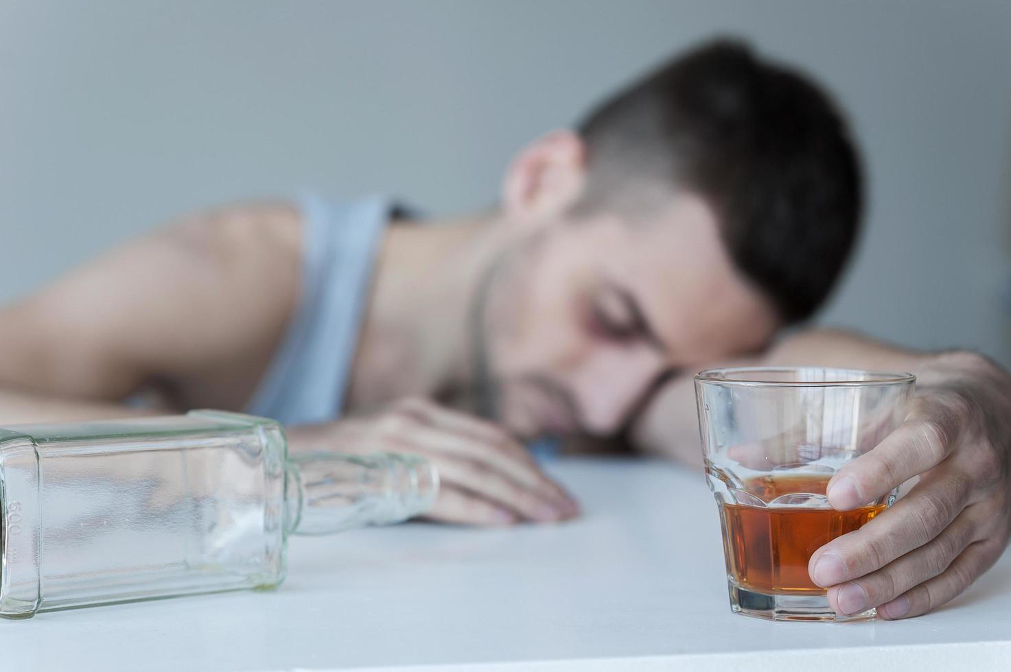 Forgetting his problems. Young man sitting at the table with empty bottle on it and keeping eyes closed photo