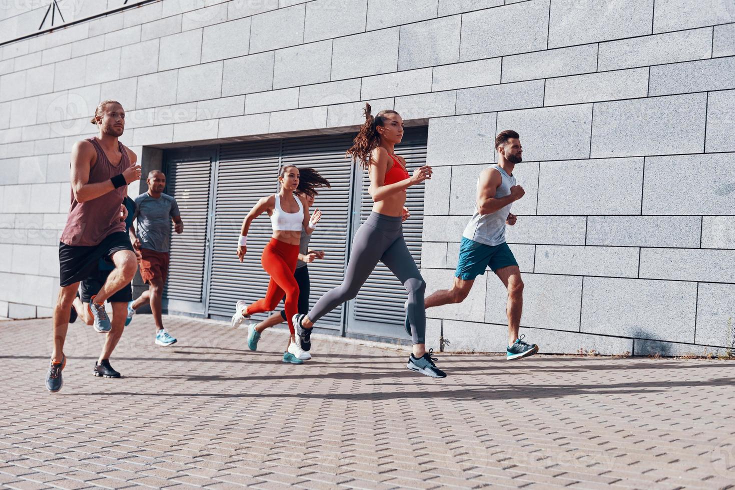 toda la longitud de los jóvenes con ropa deportiva trotando mientras hacen ejercicio en la acera al aire libre foto