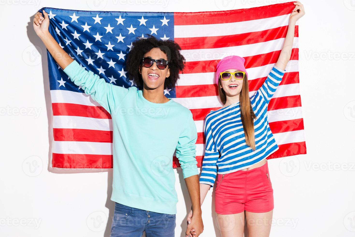 estilo americano. pareja joven funky sonriendo y mirando a la cámara mientras está de pie contra la bandera americana foto