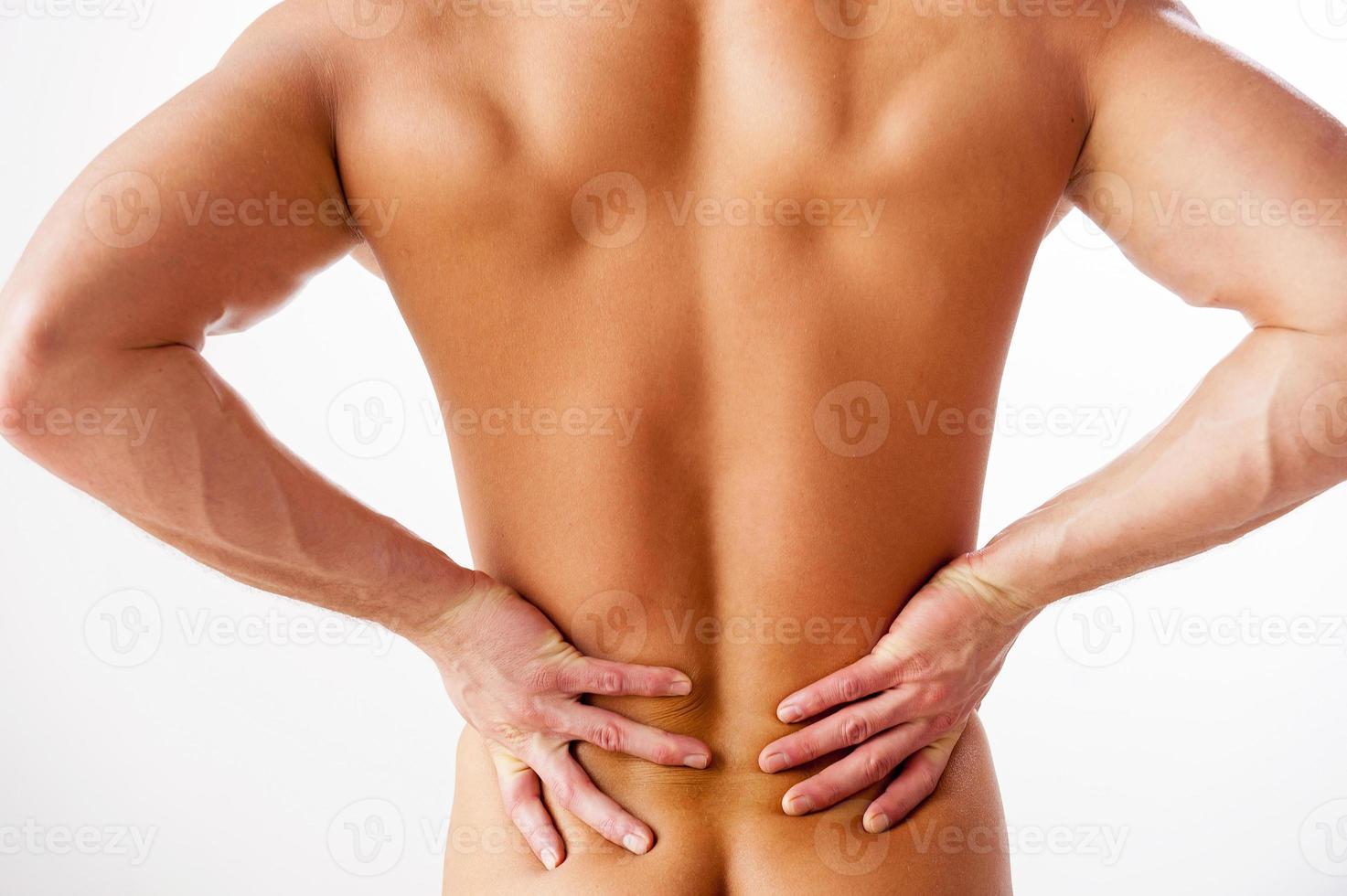 Backache. Rear view of young muscular man touching his back while standing against white background photo