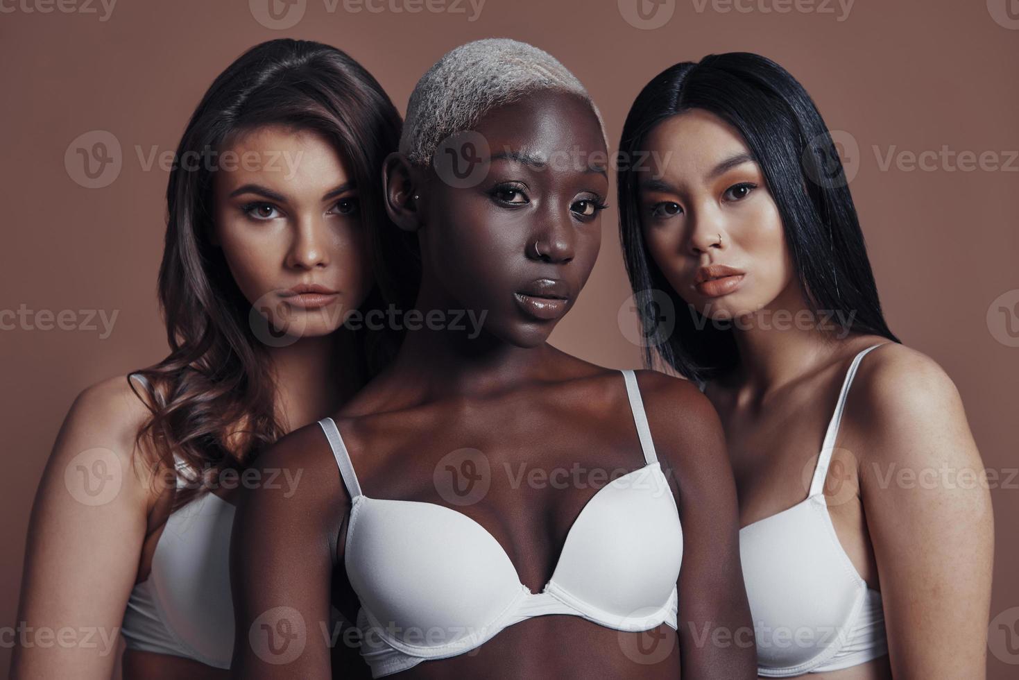 Pure beauty. Three attractive young women looking at camera while standing against brown background photo