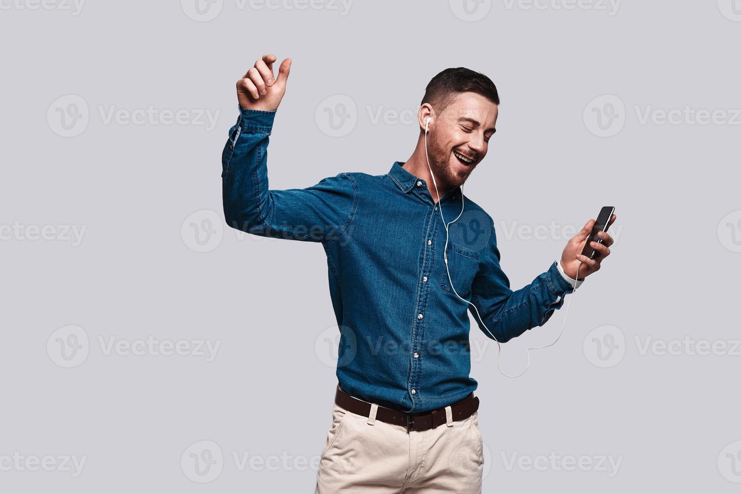 Music in heart. Handsome young man listening music and smiling while standing against grey background photo