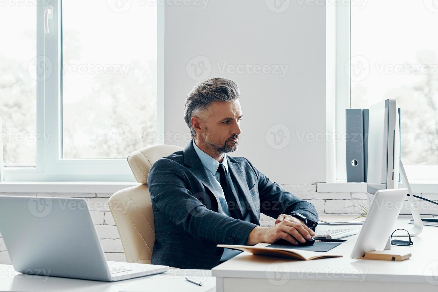 Confident mature man in formal business wear using computer while sitting at his working place photo