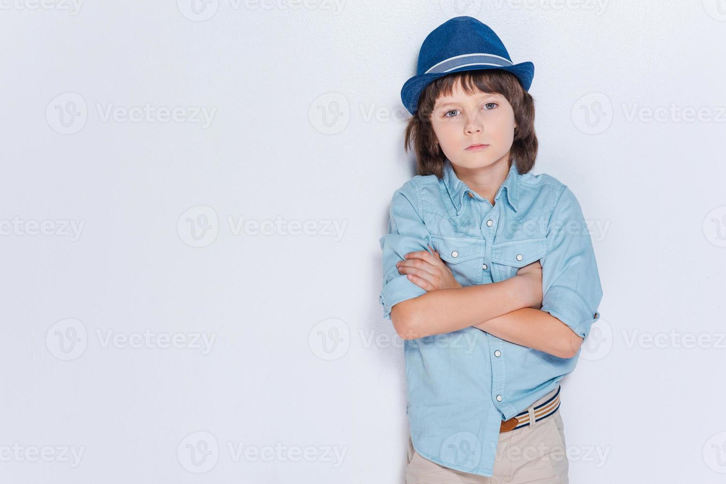 Full of inspiration.  Little boy wearing hat and keeping arms crossed while standing against white background photo
