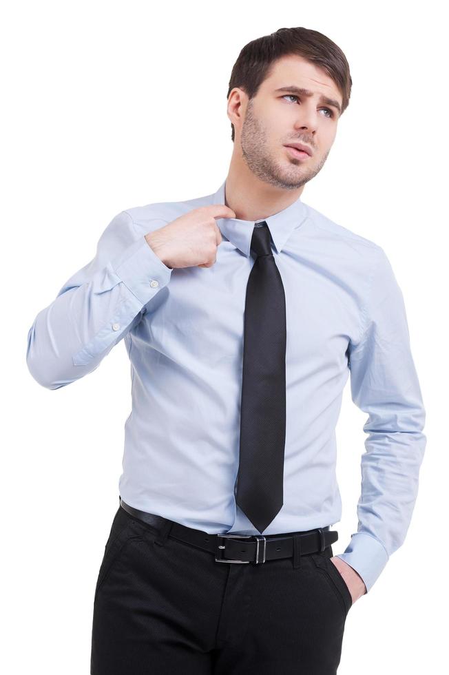 Uncertainty. Frustrated young man in shirt and tie holding hand ion hair while standing isolated on white photo