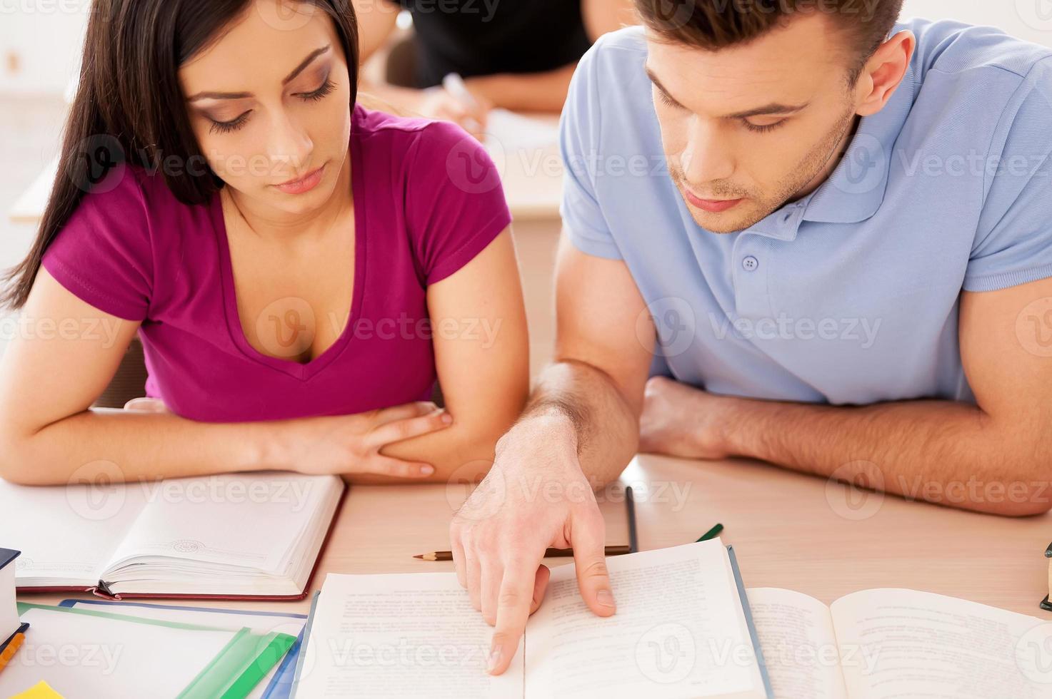 Reading a book together. Top view of two confident students reading a book together while sitting at the classroom photo