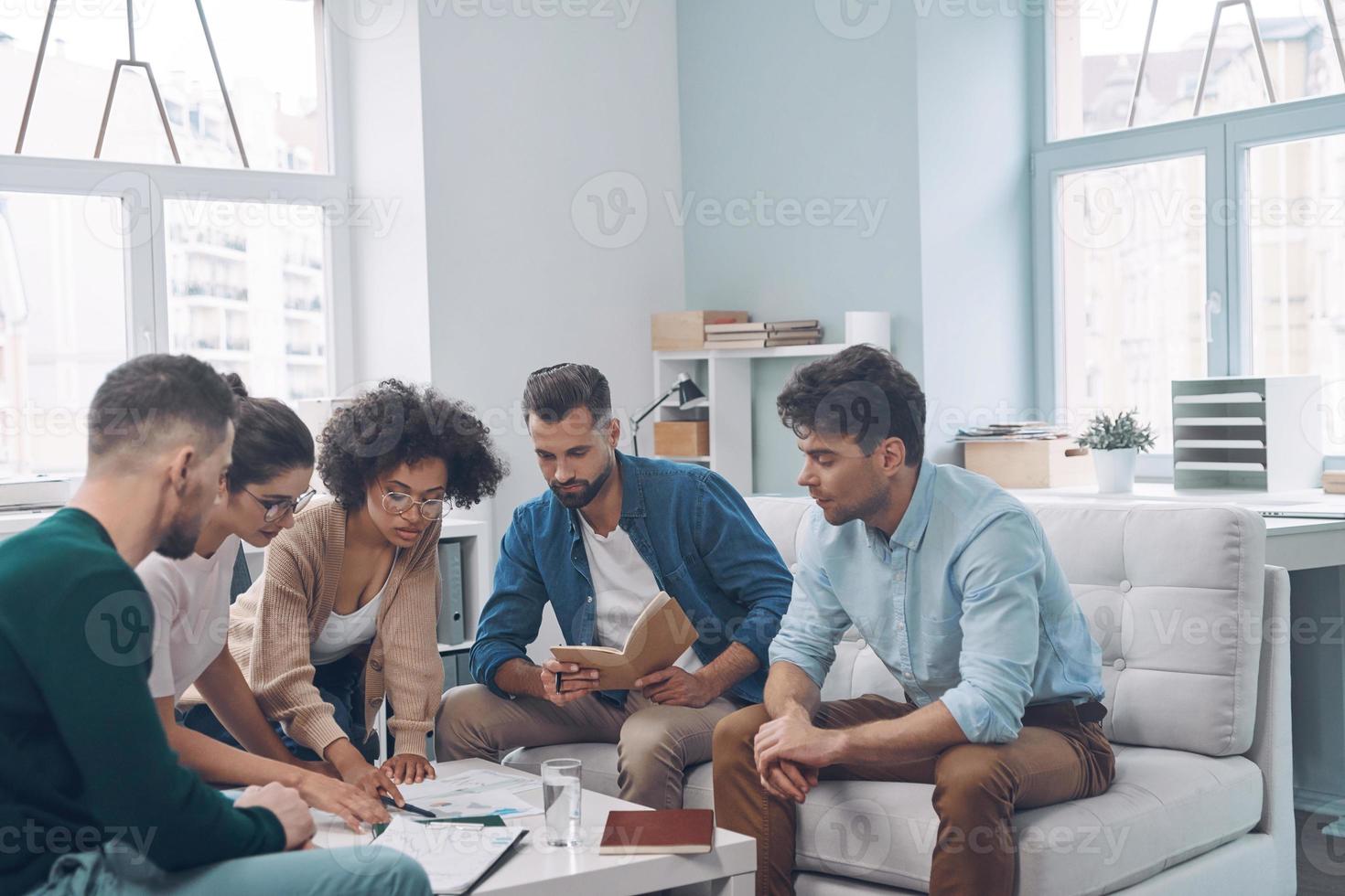 Group of modern young people discussing business while sitting in the office together photo