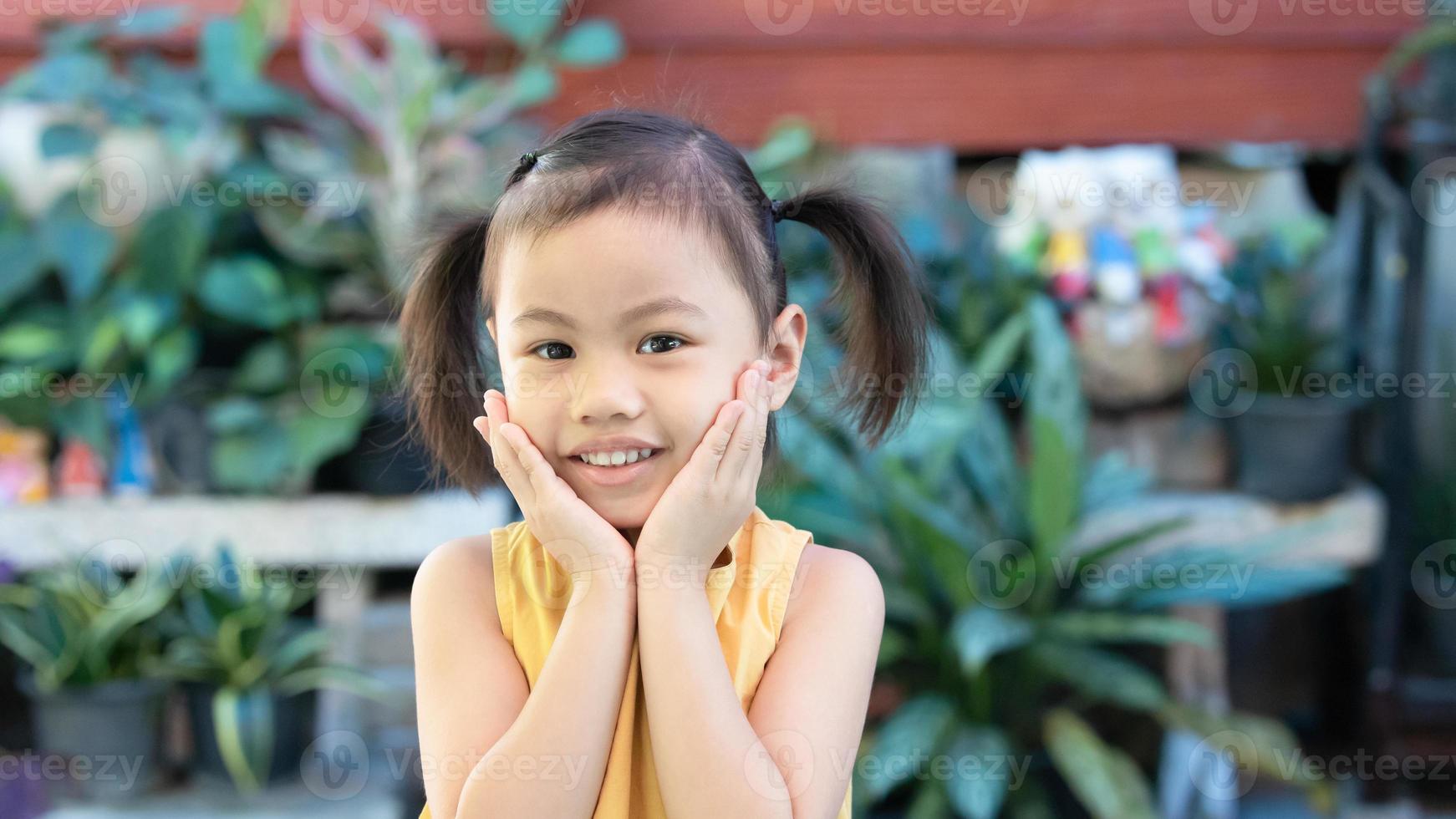 positivo encantador 4 años lindo bebé niña asiática, pequeño niño en edad preescolar con adorable pelo de coletas sonriendo mirando a la cámara foto