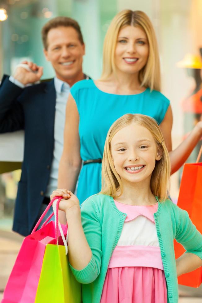 comprar juntos es divertido. familia alegre sosteniendo bolsas de compras y sonriendo a la cámara mientras está de pie en el centro comercial foto