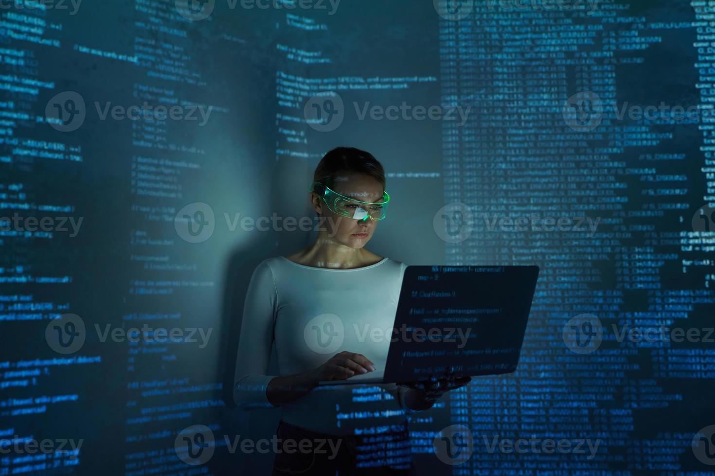 Confident woman in futuristic glasses using computer against dark background photo