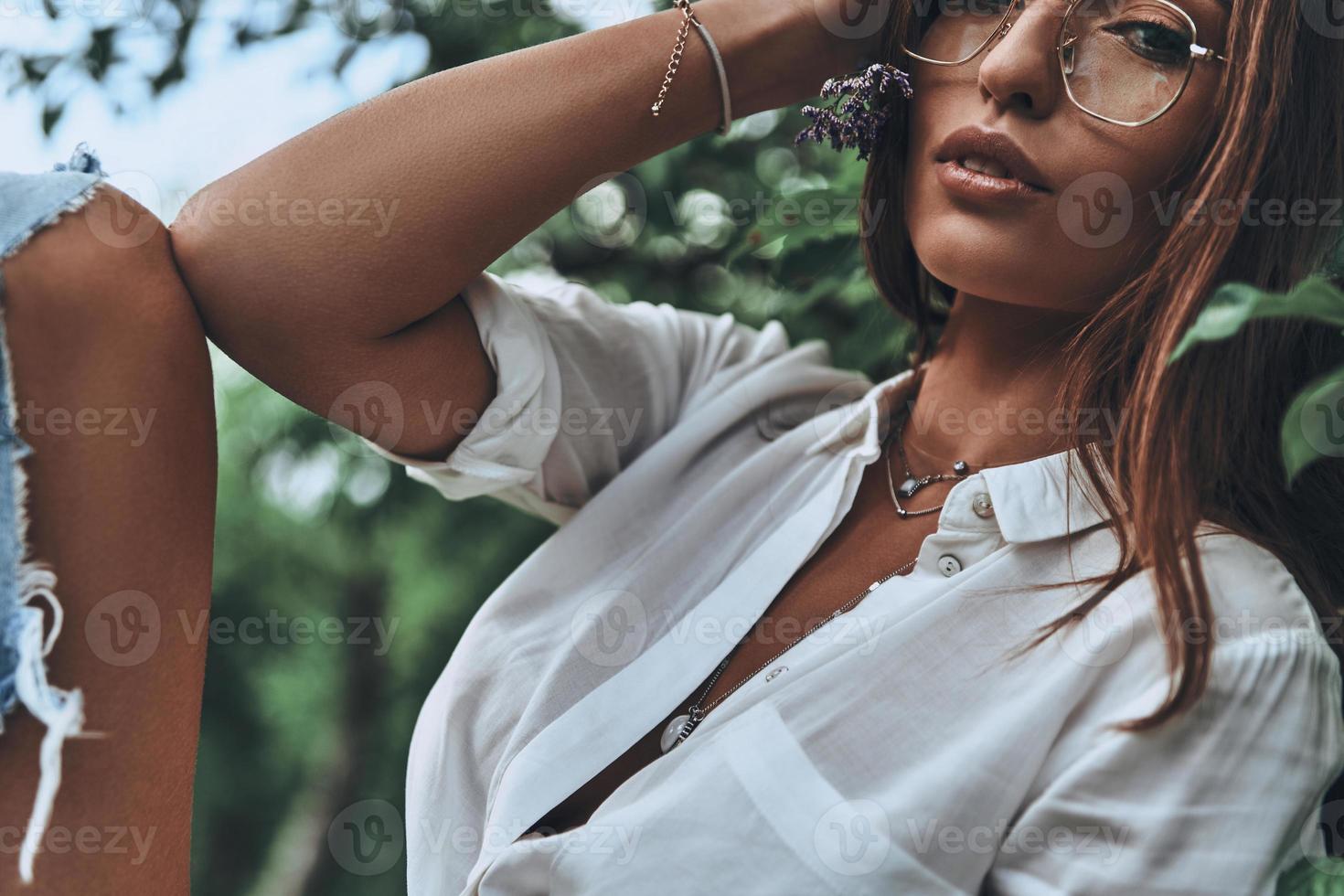 Supremely sensual.  Close-up of young attractive woman in eyewear looking at camera and keeping hand in hair while spending time outdoors photo