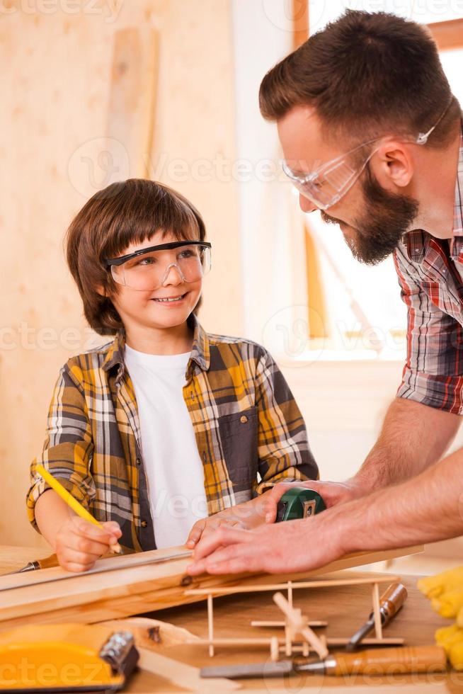 Creative minds at work.Smiling young male carpenter and his son looking at each other while working in workshop photo