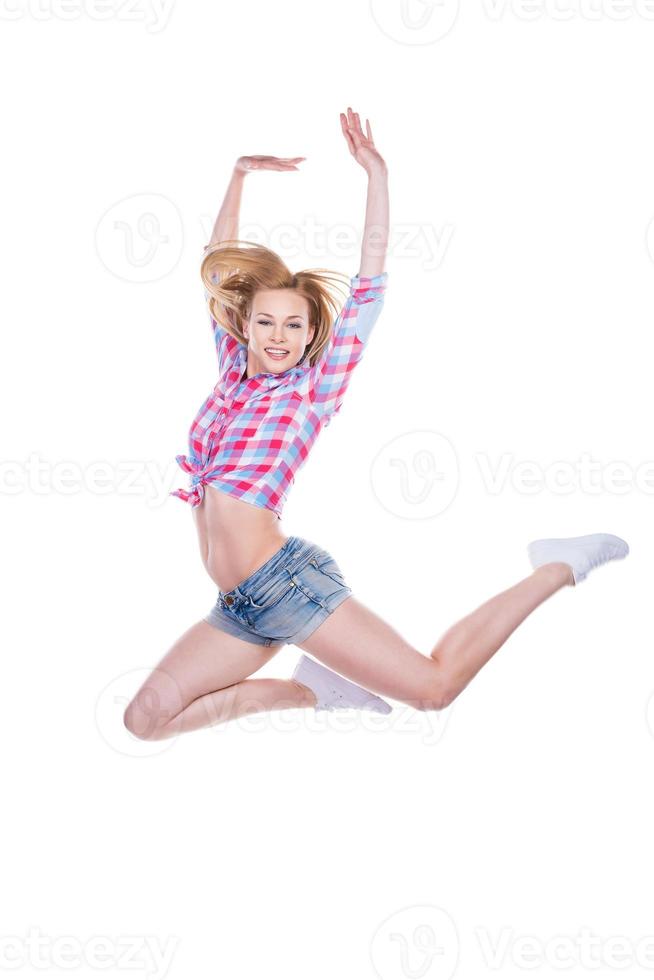 como un cisne Atractiva mujer joven con ropa funky sonriendo y mirando a la cámara mientras salta contra el fondo blanco. foto