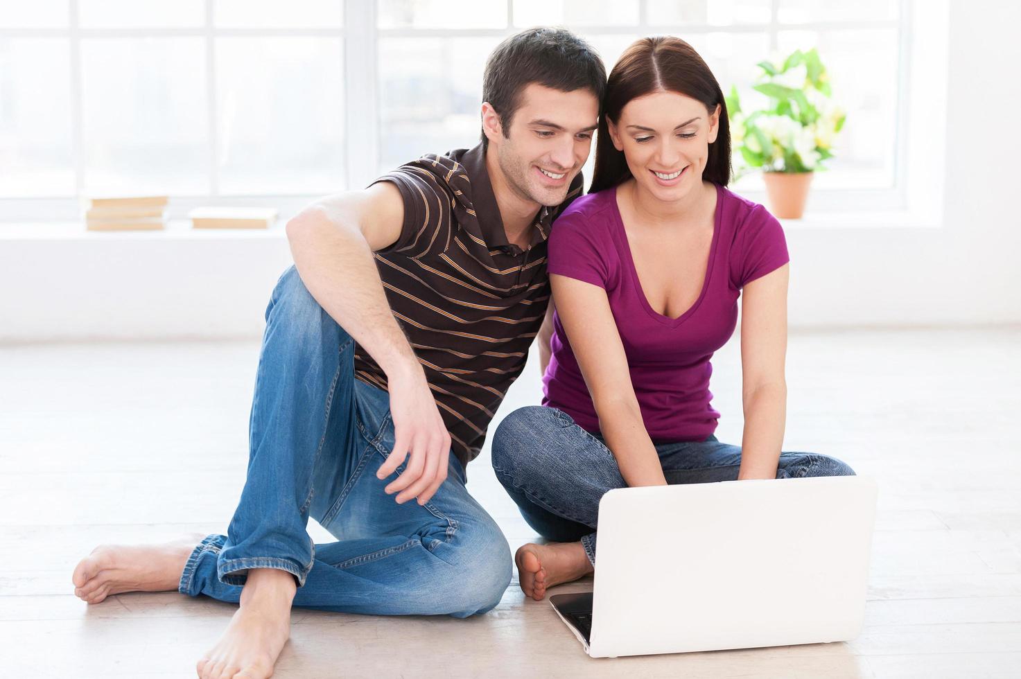 Working at their laptop. Beautiful young couple working on laptop together while sitting on the floor at their apartments photo