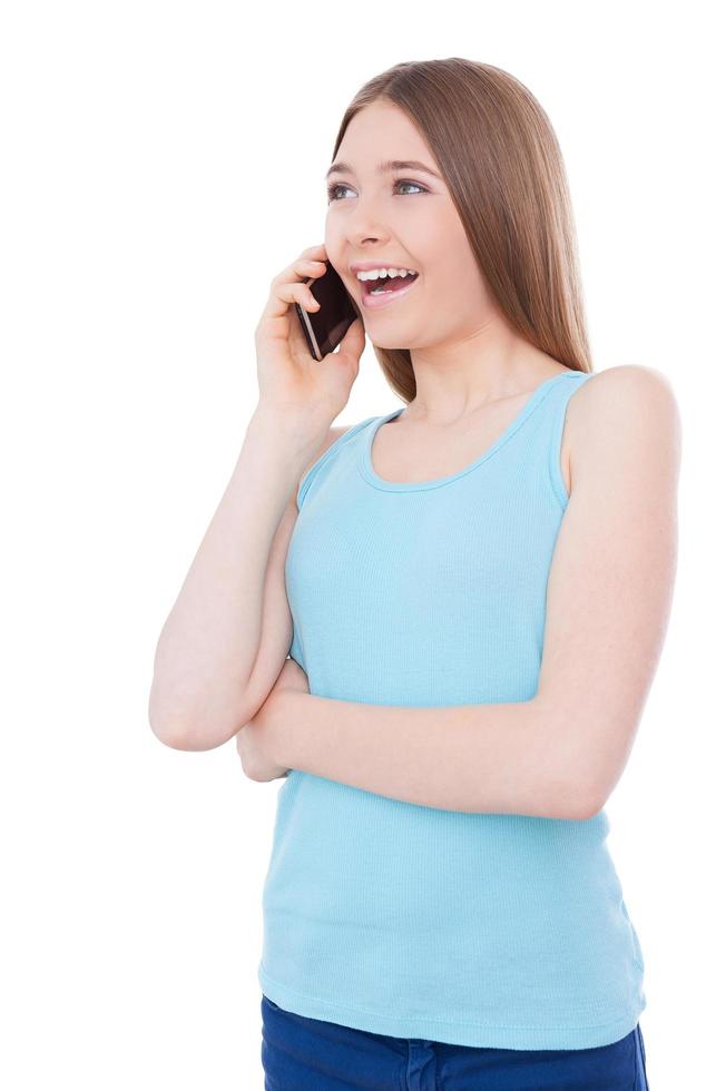 Talking with boyfriend. Cheerful teenage girl talking on the mobile phone and smiling while standing isolated on white photo