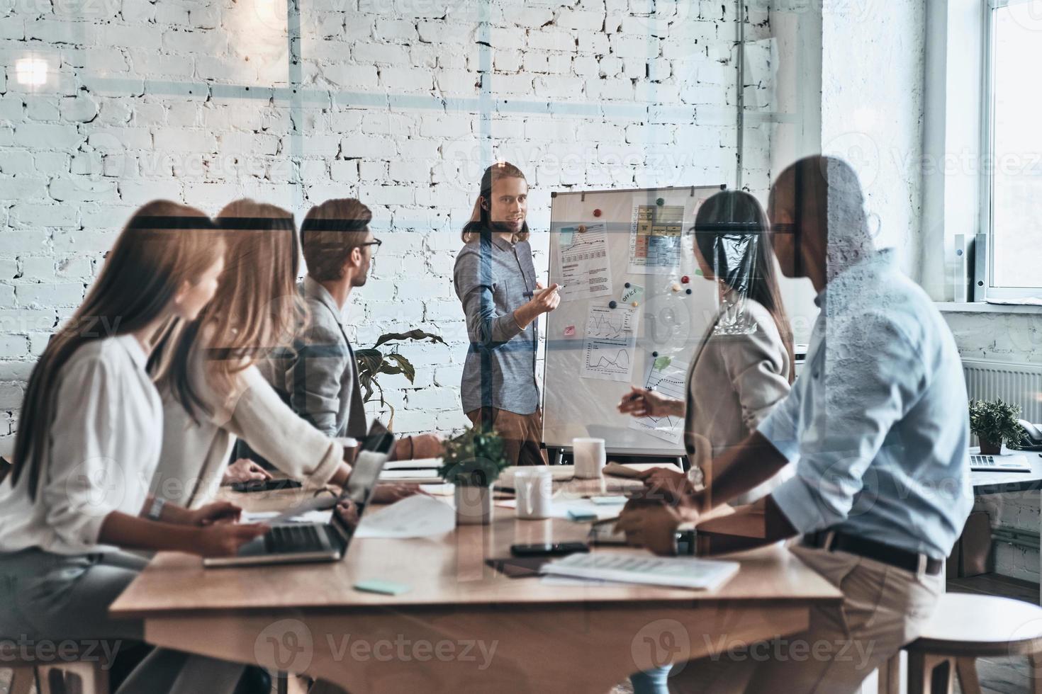 Interesting presentation. Modern young man conducting a business presentation while standing behind the glass wall in the board room photo