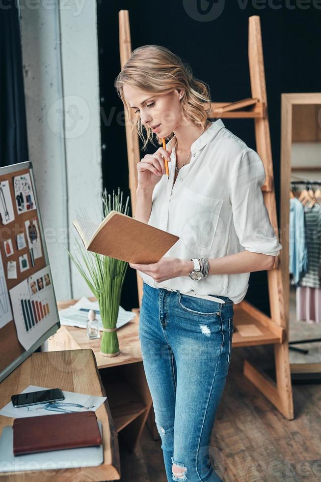 Planning the day. Thoughtful young woman looking in her personal organizer while standing in the workshop photo