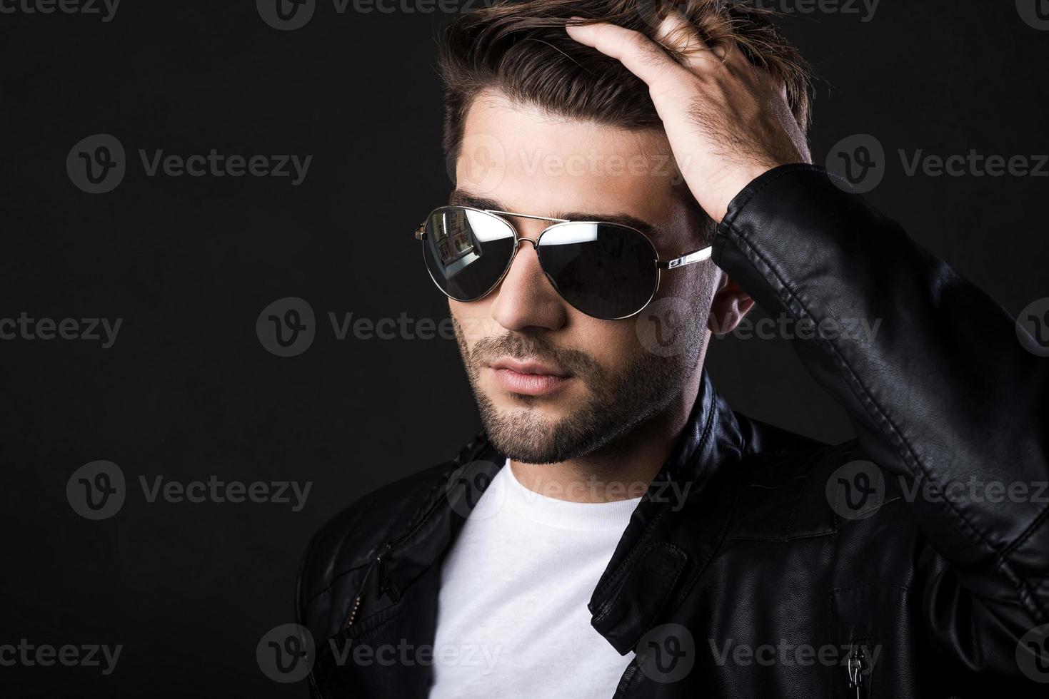 Used to look perfect. Handsome young man holding hand in hair and looking at camera while standing against black background photo