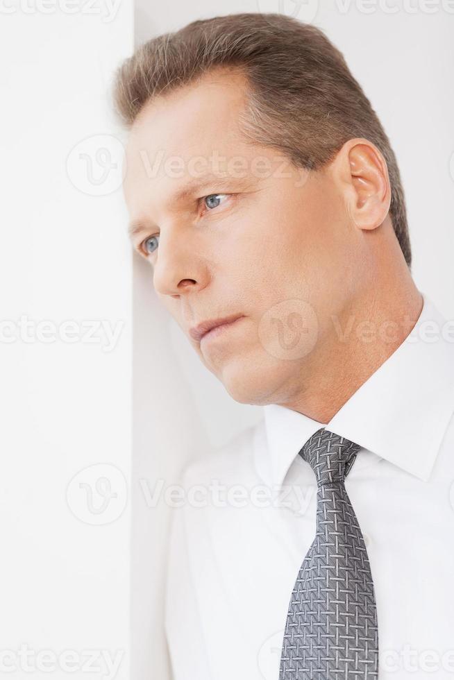 esperando inspiración. hombre maduro pensativo con camisa y corbata apoyado en la pared y mirando hacia otro lado foto