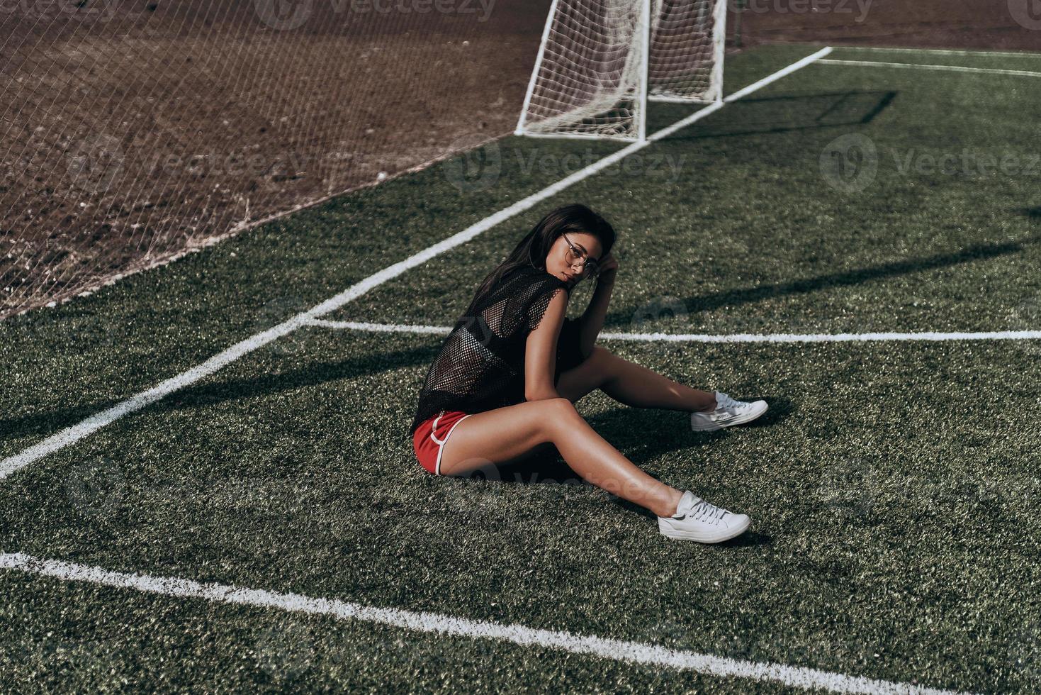 Beauty on soccer field. Beautiful young woman in sport clothing looking at camera while sitting on the soccer field photo