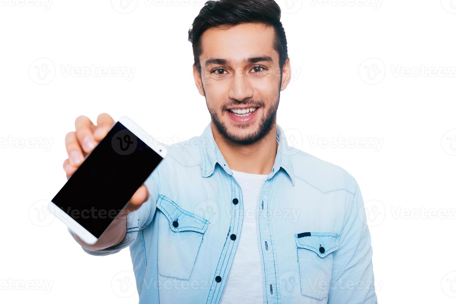 Copy space on his smart phone. Confident young Indian man showing his smart phone and smiling while standing against white background photo