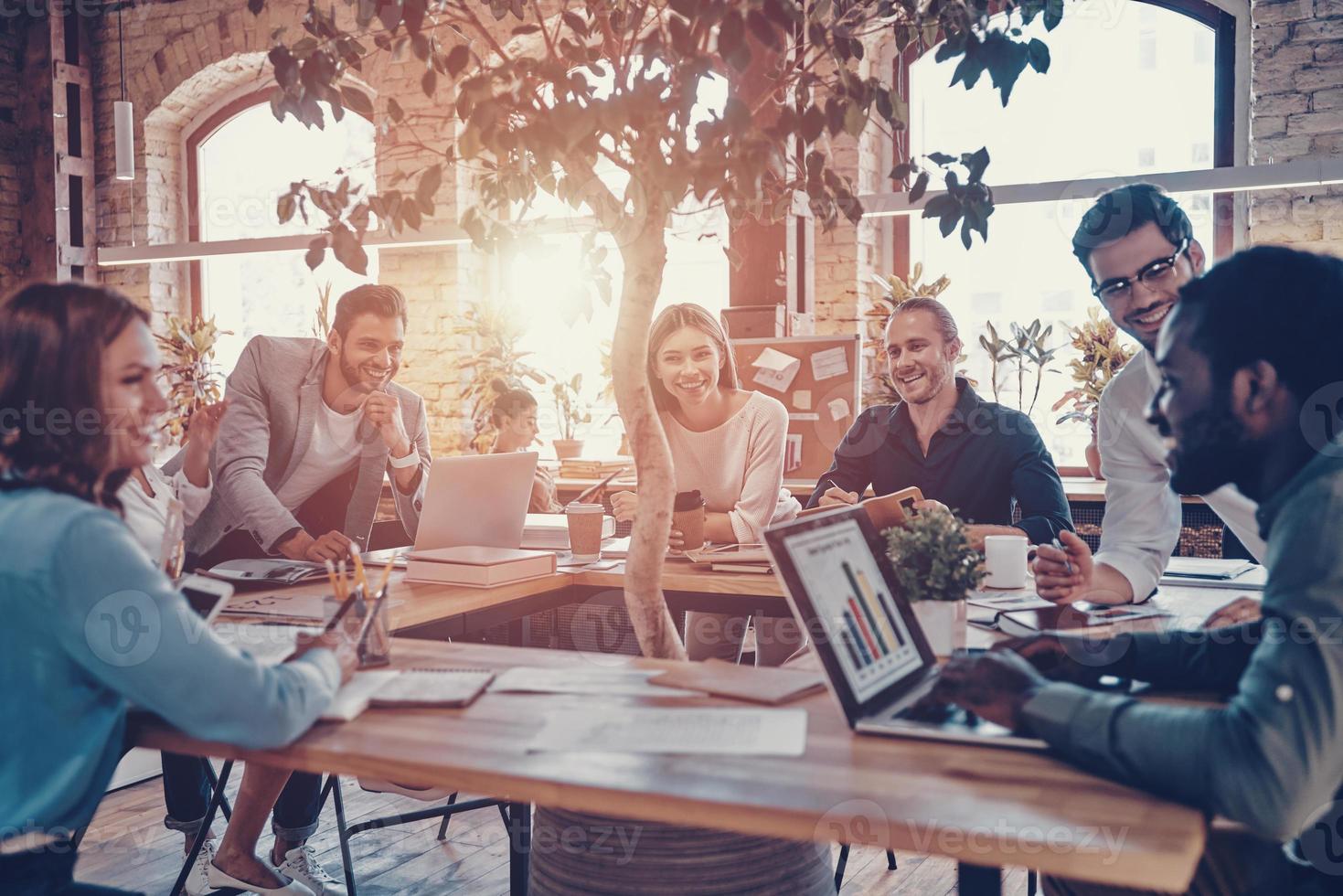 Group of young modern people in smart casual wear communicating and using modern technologies while working in the office photo