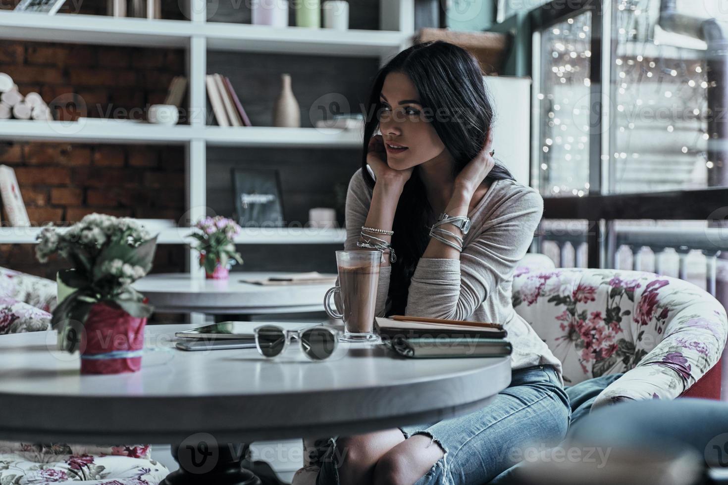 bella soñadora. mujer joven atractiva mirando hacia otro lado con una sonrisa mientras se sienta en el restaurante foto