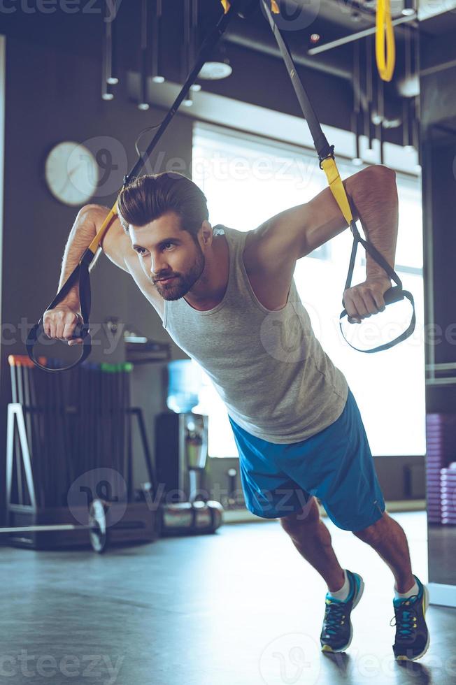 Strength and power. Full-length of young man in sportswear exercising at gym photo