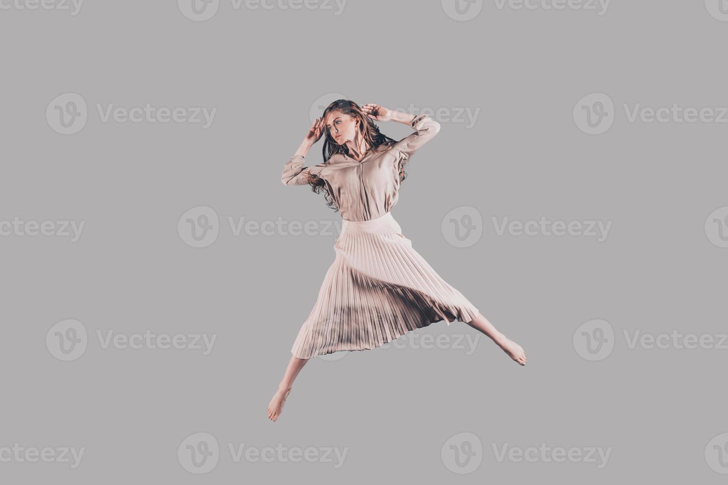 Jumping so high. Studio shot of attractive young woman in beautiful dress hovering in air photo