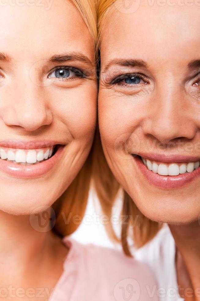 Daughter with mother. Close-up of mother and her daughter smiling and looking at camera while standing cheek to cheek against white background photo