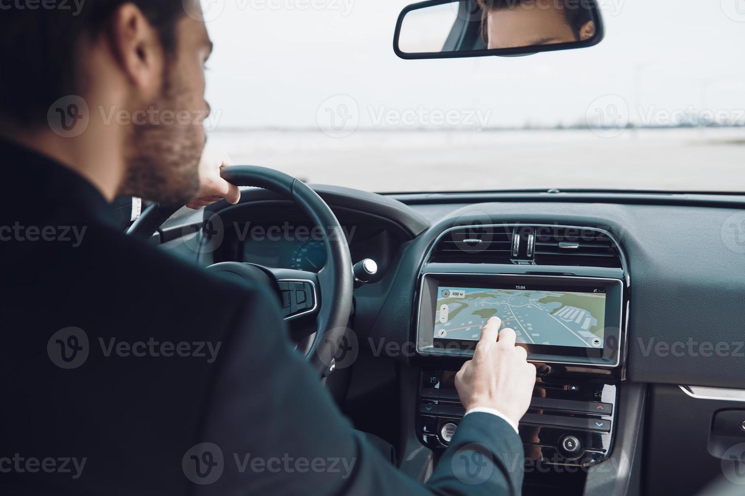Getting around the city. Rear view of young man in full suit using global positioning system device to check the map while driving a car photo