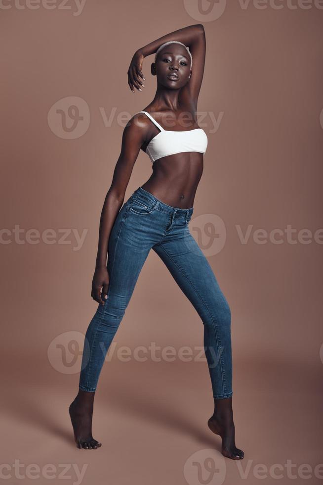 Feeling beautiful. Full length of attractive young African woman looking at camera while standing against brown background photo