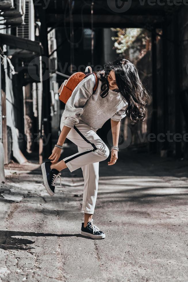 Perfect style. Beautiful young woman adjusting her shoe and looking away while standing outdoors photo