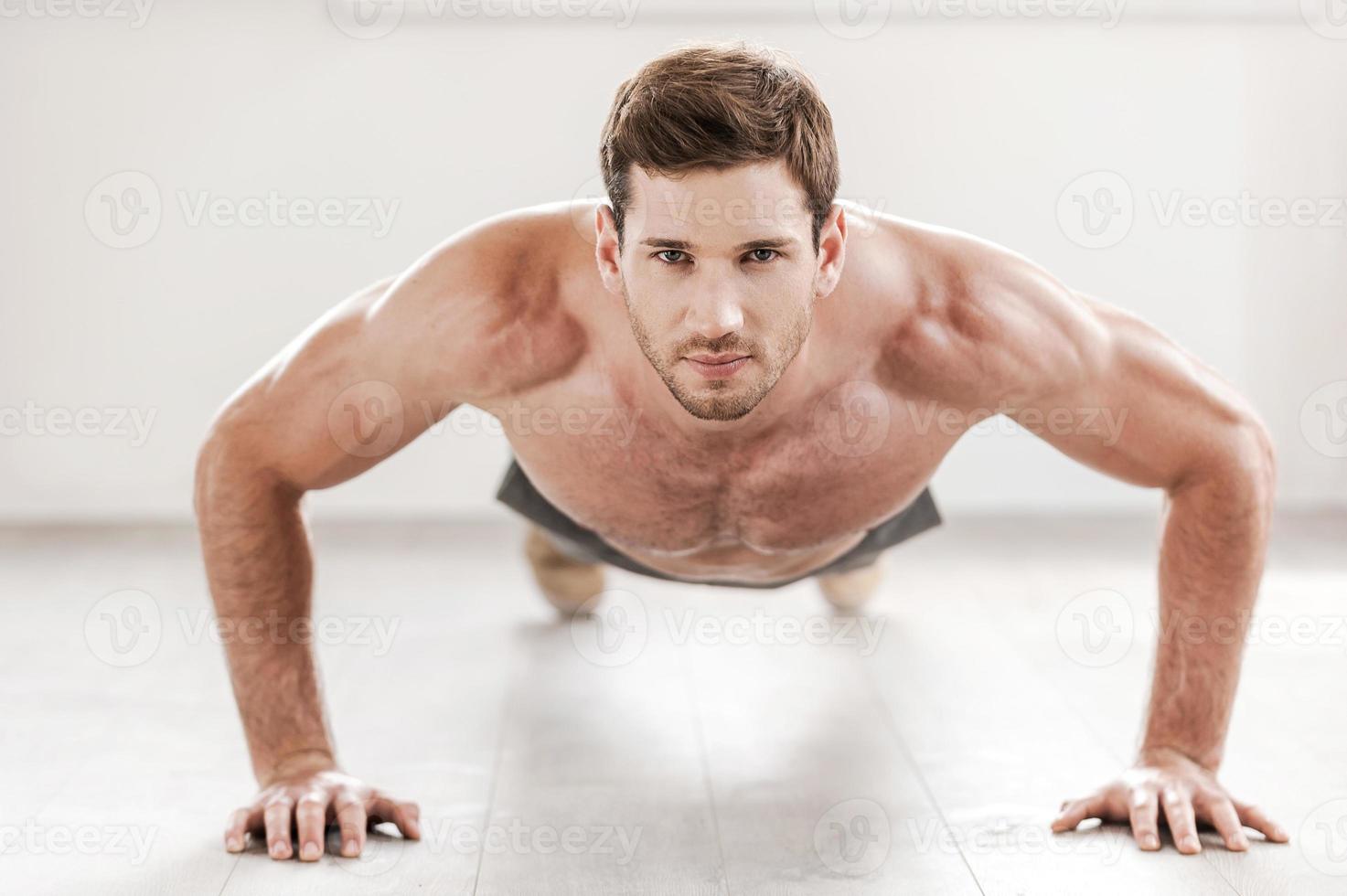 Confident man doing push-ups. Confident young muscular man doing push-ups and looking at camera photo