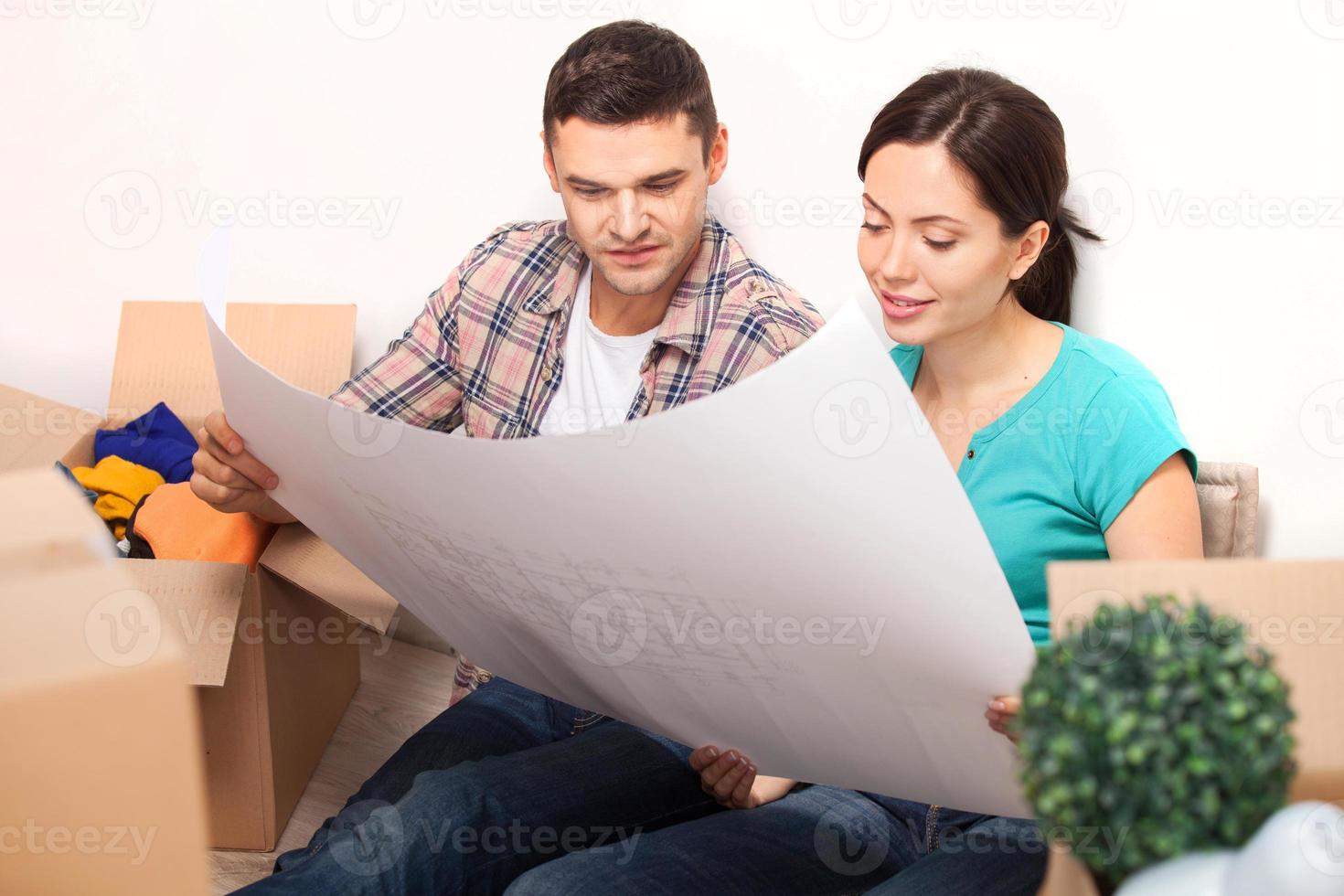Examining a blueprint. Beautiful young couple sitting on the floor and looking at the blueprint while cardboard boxes laying around them photo