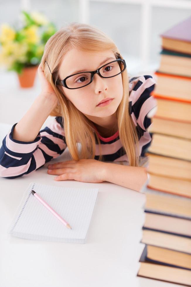 cansado de estudiar. niña cansada mirando la pila de libros y sosteniendo la cabeza en la mano mientras se sienta en la mesa foto