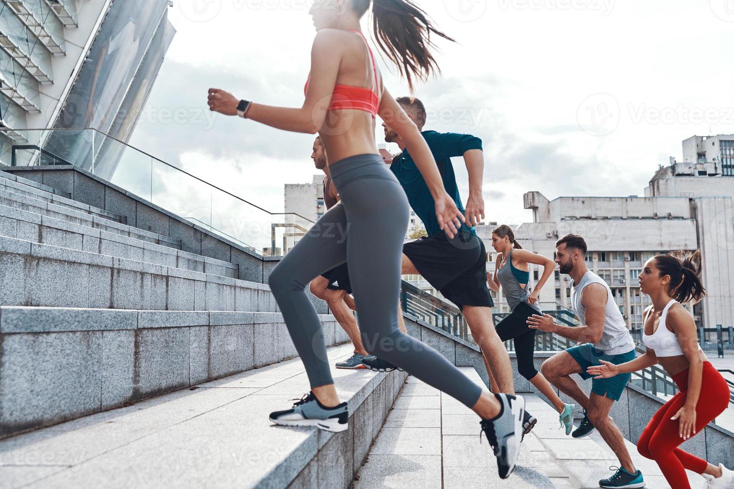 Group of young people in sports clothing jogging while exercising on the stairs outdoors photo