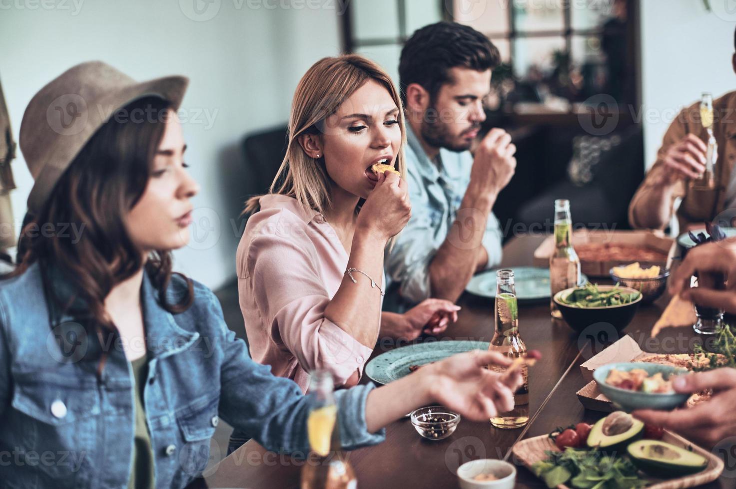 dejar todas las preocupaciones atrás. grupo de jóvenes con ropa informal comiendo mientras cenan en el interior foto