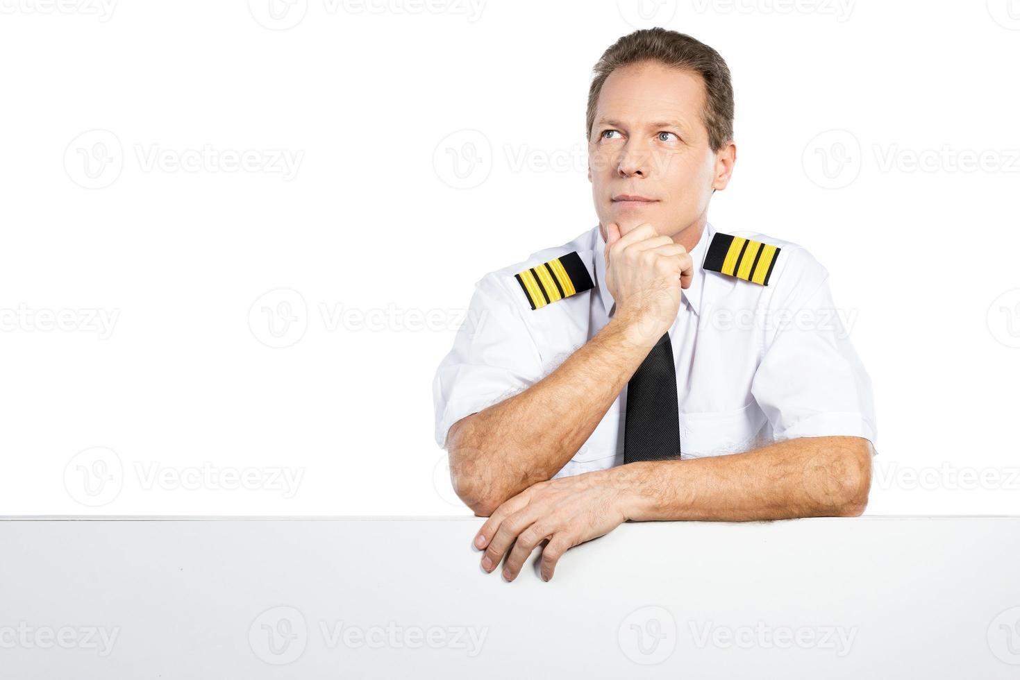 piloto pensativo. piloto masculino pensativo en uniforme apoyado en el espacio de la copia y mirando hacia otro lado mientras está de pie contra el fondo blanco foto